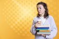 Bookworm holding pile of novels and caffeinated drink early in the morning