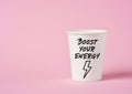 Boost your energy message on a paper coffee cup on pink background. Caffeine and energy boost concept Royalty Free Stock Photo
