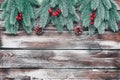 A border of decorative spruce branches with holly and a pine cone on a dark wooden plank background. Christmas Royalty Free Stock Photo