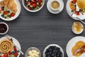 A border of delicious breakfast plates, pancakes and pasteries, bowls of fruit, jam and butter, and a cup of coffee, on a dark Royalty Free Stock Photo