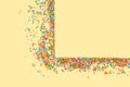 Border frame of colorful sprinkles on a yellow background with c