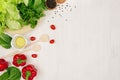 Border of fresh green greens, red paprika, cherry tomato, pepper, oil and utensils on soft white wooden background. Royalty Free Stock Photo