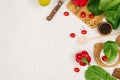 Border of fresh green greens, red paprika, cherry tomato, pepper, oil and utensils on soft white wooden background. Royalty Free Stock Photo