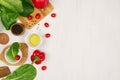 Border of fresh green greens, red paprika, cherry tomato, pepper, oil and utensils on soft white wooden background. Royalty Free Stock Photo