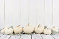 Border of white pumpkins and leaves, white wood background