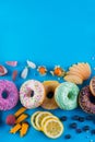 Bordure of colorful fresh donuts with different kinds of topping and fruits on blue paper background.