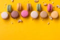Bordure of colorful macaroons and nuts on yellow background. Sweet macarons with. Top view.