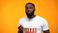 Bored Afro-American man with popcorn watching uninteresting TV program, close-up