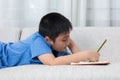 Bored Asian Chinese little boy writing book on the sofa