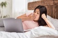 Bored Asian Girl Using Laptop Lying In Bed At Home