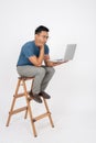 A bored Asian man is waiting for an email on his laptop while sitting on a wooden ladder. isolated Royalty Free Stock Photo