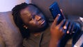 Bored black man using smartphone while resting on the couch