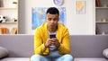 Bored black teenage guy scrolling smartphone, wasting time in social network