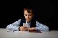 Bored boy pupil watching phone at the lesson in the dark room.