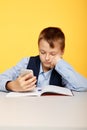 Bored boy pupil watching phone at the lesson in the yellow classroom. Royalty Free Stock Photo