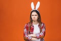 Bored bunny. Angry young caucasian woman in bunny ears while standing against orange background. Isolated