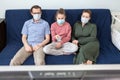 A bored Caucasian family wearing medical masks sitting on sofa at home watching television, teenager girl with tv remote control Royalty Free Stock Photo