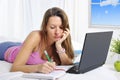 Bored college student girl lying on bed with computer studying for exam Royalty Free Stock Photo