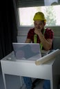 Bored construction Worker is sitting at his desk at the computer, looking at building plans AND counting.