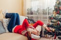 Bored disappointed young woman lying on couch by Christmas tree in Santa hat feeling sad, upset, lonely Royalty Free Stock Photo