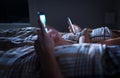 Bored distant couple ignoring each other lying in bed at night while using mobile phones. Smartphone addict. Royalty Free Stock Photo