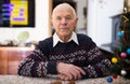 bored elderly man sitting alone at table with small Christmas tree. Royalty Free Stock Photo