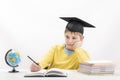 Bored elementary schoolboy does homework at home. Boy in the students hat writes in notebook. Child is tired of learning