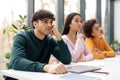 Bored european student guy leaning on hand and listening lecture, sitting with classmates at table in classroom Royalty Free Stock Photo