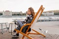 Bored european woman in black shoes sitting on recliner and playing with her hair. Outdoor portrait of serious girl in