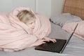 Bored girl lying in bed under blanket and learning in virtual online school or class. Kid working on laptop Internet at home. Royalty Free Stock Photo