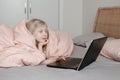 Bored girl lying in bed under blanket and learning in virtual online school class. Kid working on a laptop Internet at home. Child Royalty Free Stock Photo