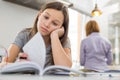 Bored girl studying at table with mother standing in background