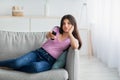 Bored Indian teen girl with remote control watching TV on sofa at home, copy space Royalty Free Stock Photo