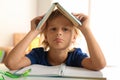 Bored little boy with book on his head doing homework at table indoors Royalty Free Stock Photo