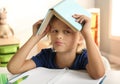 Bored little boy with book on his head doing homework at table indoors Royalty Free Stock Photo