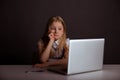 Bored little girl sitting on at the table and using computer isolated. Royalty Free Stock Photo