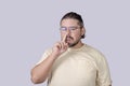 A bored man in his 30s picking his nose for a booger in an unmannerly fashion. Scene isolated on a gray background