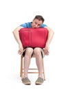 Bored man in shorts and a t-shirt with a red suitcase sits on a chair waiting, isolated on white background. Front view Royalty Free Stock Photo