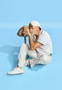 Bored. Portrait of handsome senior man in stylish white outfit sitting, leaning head on tennis racket over blue