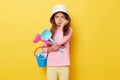 Bored sad little girl wearing casual clothing and panama holding sandbox toys and bucket isolated over yellow background feeling Royalty Free Stock Photo