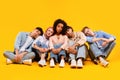 Bored sad multiracial students sitting on floor in line and putting heads on friends shoulders over yellow background