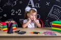 Bored schoolgirl sitting at the desk with books, school supplies, holding her both hands over the cheecks, looking to Royalty Free Stock Photo
