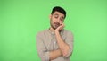 Bored sleepy brunette man standing leaning on his hand and looking at camera with disinterest. green background, chroma key