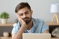 Bored sleepy man feels drowsy resting on hand near laptop