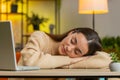Bored sleepy business woman worker works on laptop leaning on hands falling asleep at home table Royalty Free Stock Photo
