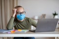 Bored teen girl in face mask using laptop, studying online