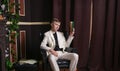 Bored teen student guy in white business suit sitting in a chair with a book by the fireplace Royalty Free Stock Photo