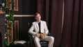 Bored teen student guy in white business suit sitting in a chair with a book by the fireplace Royalty Free Stock Photo