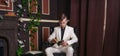 Bored teen student guy in white business suit sitting in a chair with a book by the fireplace Royalty Free Stock Photo