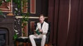 Bored teen student guy in white business suit sitting in a chair with a book by the fireplace Royalty Free Stock Photo